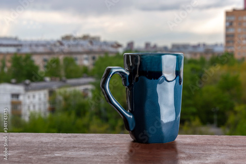 Blue mug on a wooden table in the patio against the background of the cityscape.