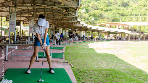 Healthy Sport.  Asian sporty woman swing golf ball practice at golf driving range on evening on time for healthy sport. Lifestyle and Sport Concept
