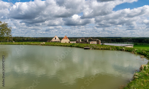 landscape with a small pond and ancient buildings on its shore, gorgeous cumulus clouds