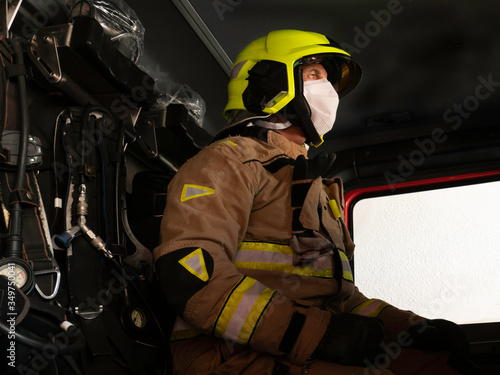 Firefighter sitting in the truck with helmet and mask to protect himself from the covid 19.