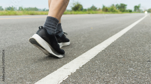 Fototapeta Naklejka Na Ścianę i Meble -  The legs of male athletes in black shoes are preparing to run on the paved road Outdoor exercise for weight loss and good health.Fitness and healthy lifestyle Competition and successful concept.