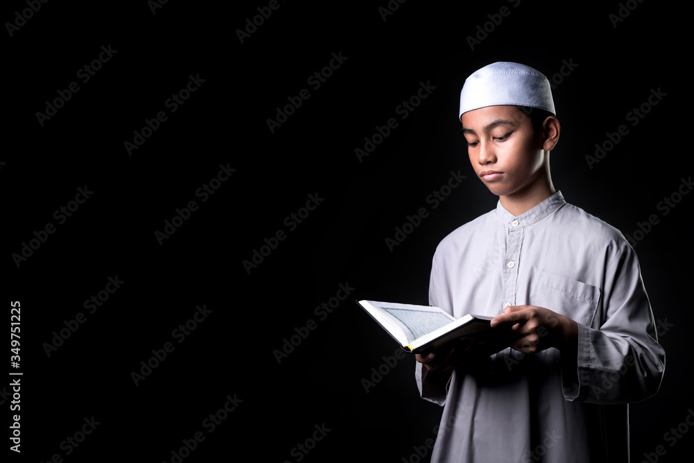 Portrait A Muslim boy in Asian Islam is standing and reading the Quran and appreciates on black background, with copy space. Portrait A Muslim boy in Asian Islam is standing and reading the Quran and appreciates on black background, with copy space.