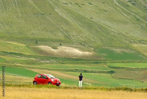 A man next to a small red car stopped on the plateau of Castelluccio di Norcia.Umbria, Italy.