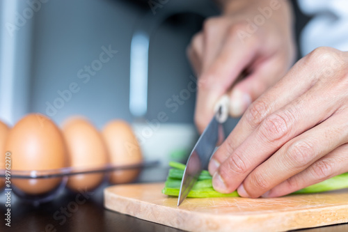 closeup of people hand and knife slice spring onion on wood butcher and fresh chicken egg in bowl and group of egg in box on wooden kitchen table for healthy and delicious meal or food dinner cook