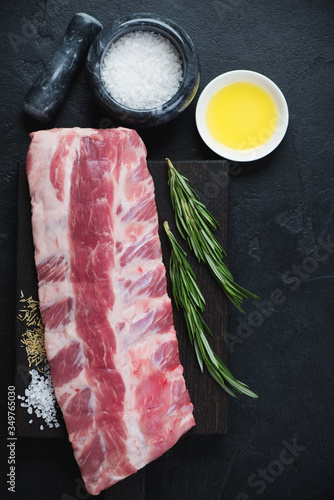 Above view of raw pork ribs and seasonings over black stone background, vertical shot