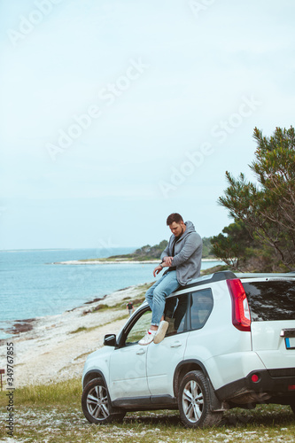 man sitting on the car roof enjoying view of summer sea © phpetrunina14