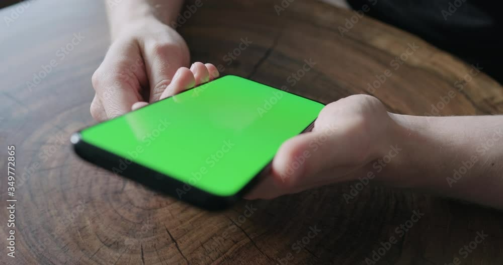 Closeup young man use smartphone with green screen while sitting at the table Closeup young man use smartphone with green screen while sitting at the table