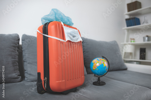 Travel bag suitcase with earth globe, mask and head protection from viruses and flu influenza. Tourist traveling canceled all over the world, 2020. season is postponed.