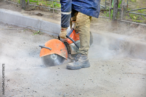 A construction worker using a portable gasoline saw cuts old asphalt to repair a site on the road.