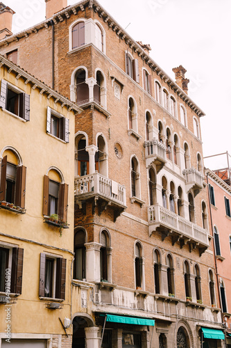 Closeup of the facade of a building, on the streets of Venice, Italy. Five-story stone building with white balconies with columns, classic Venetian arched windows.