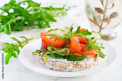 Open sandwich with crispbread salted salmon, cream cheese, sliced cucumber and arugula on plate.