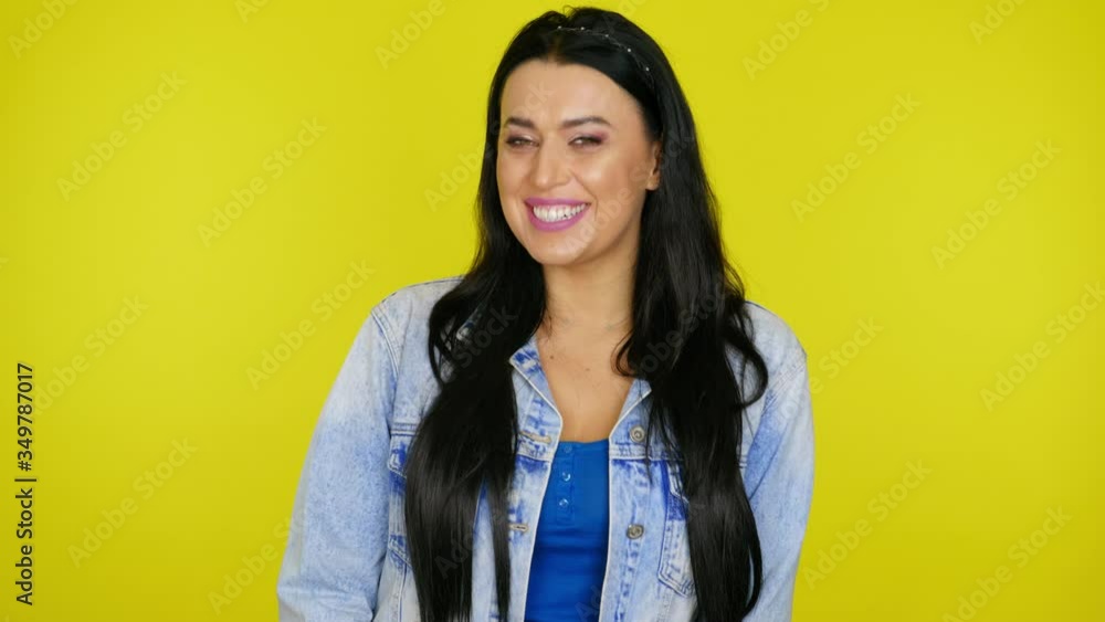 Woman with black hair in a denim jacket laughs and looks at the camera on a yellow background with copy space. Place for text or product. 4K footage Woman with black hair in a denim jacket laughs and looks at the camera on a yellow background with copy space. Place for text or product. 4K footage