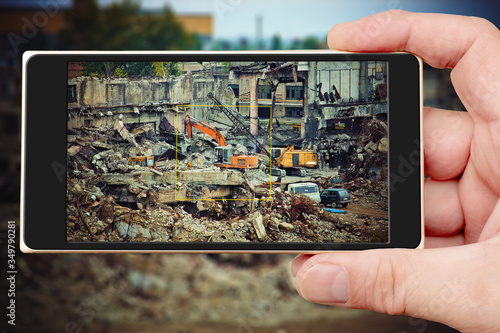 Destroyed industrial enterprise. Photos of smartphone. Smartphone in hand. Excavator on screen.