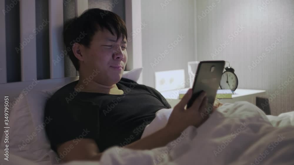 Young asian man with tablet computer lying on bed Young asian man with tablet computer lying on bed