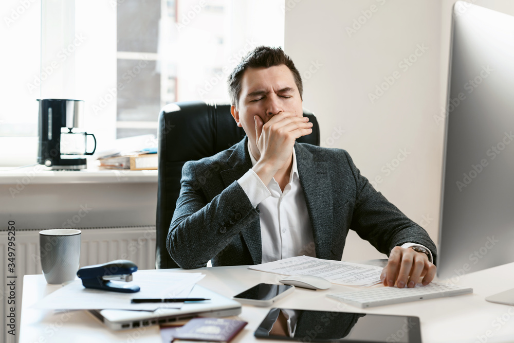 An overworked employee works on a desktop computer. Tired businessman or office worker yawns and falls asleep at the workplace. Sales manager, financial analyst or IT specialist, freelancer. An overworked employee works on a desktop computer. Tired businessman or office worker yawns and falls asleep at the workplace. Sales manager, financial analyst or IT specialist, freelancer.