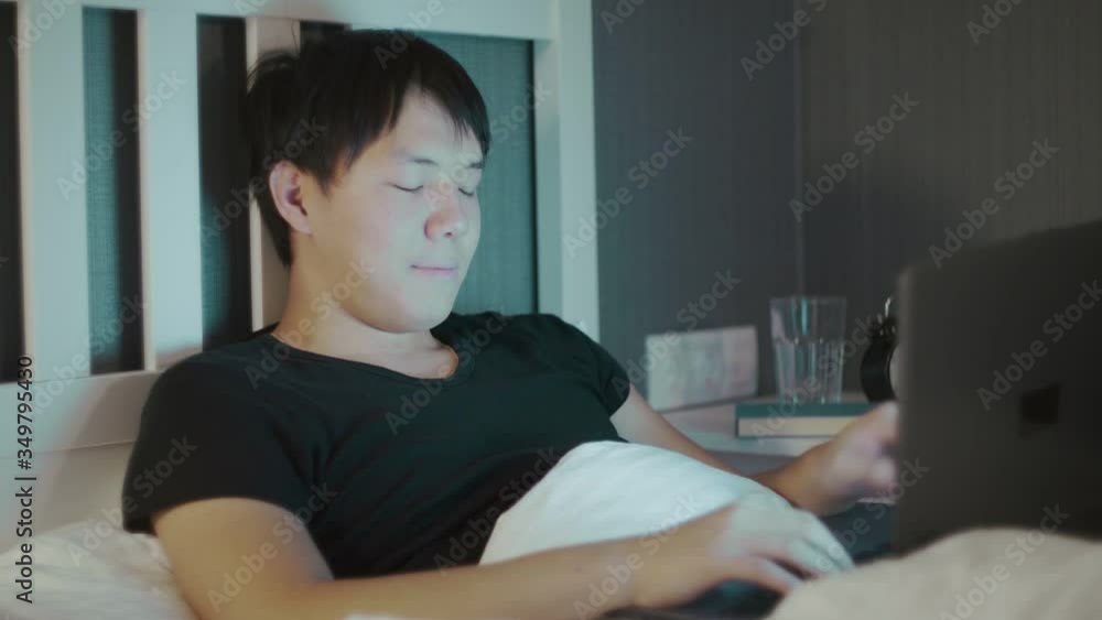 Young asian Man Using A Laptop Late At Night In Bed Young asian Man Using A Laptop Late At Night In Bed
