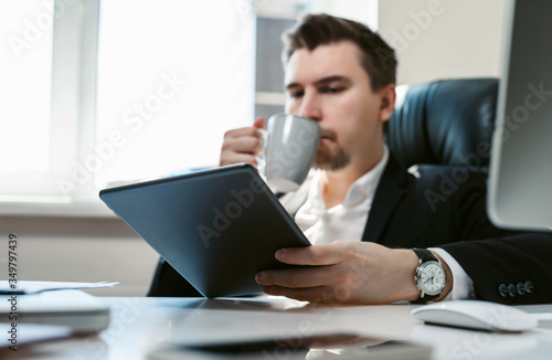 Young successful businessman and office employee reading news on his tablet. Coffee break during the working day. A financial analyst or broker studies stock market fluctuations. economic crisis 2020