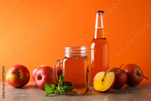 Composition with cider and apples on gray table against orange background