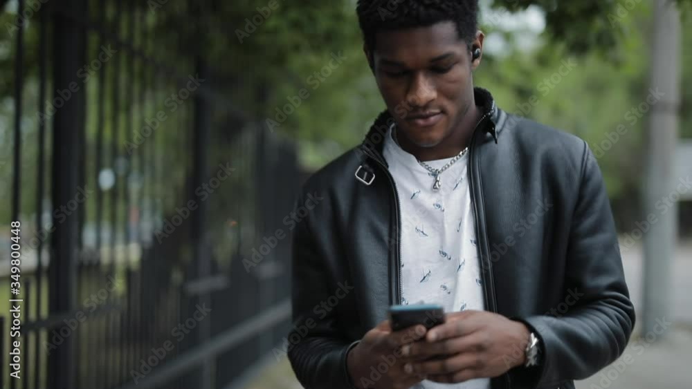 African American man looks down at smartphone walking in the summer city African American man looks down at smartphone walking in the summer city