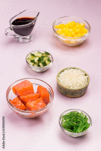 Set of raw vegetables, red fish, rice, soy sauce in glass bowls.