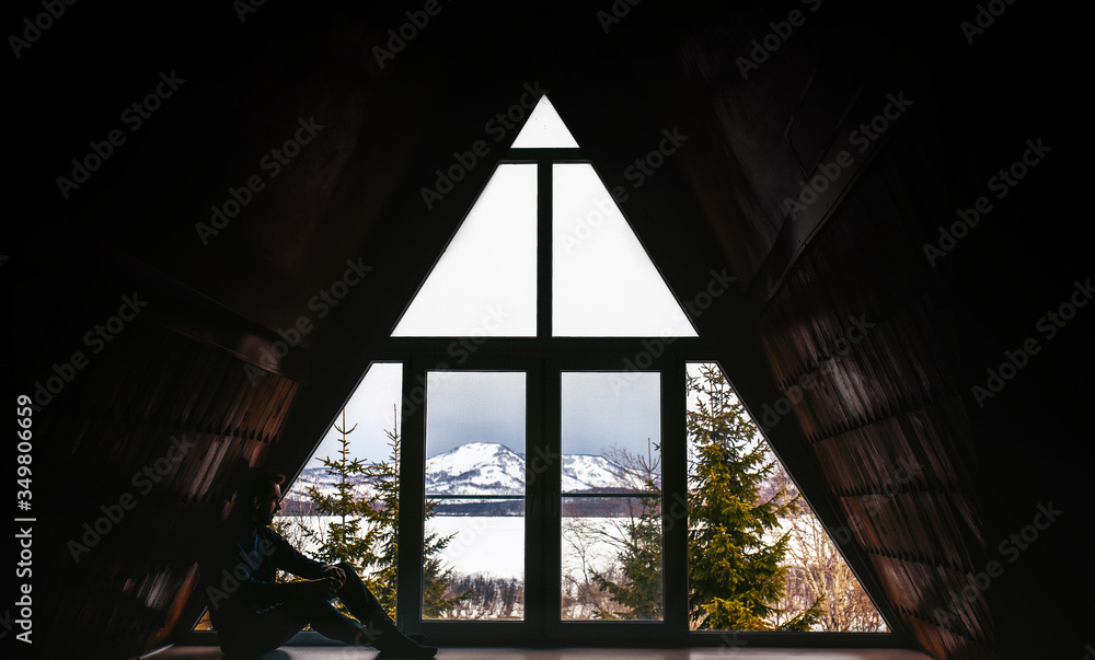 Fototapeta premium traveler relaxing near window in cozy wooden cottage with snowy mountains view.