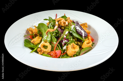 tasty squid salad with tomatoes, arugula and sauce on a white plate, isolated on a black background.