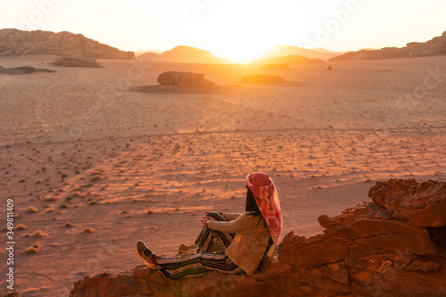 A woman traveller sitting on rock up on hill and enjoying beautiful sunset in Wadi Rum desert, Jordan, Arab