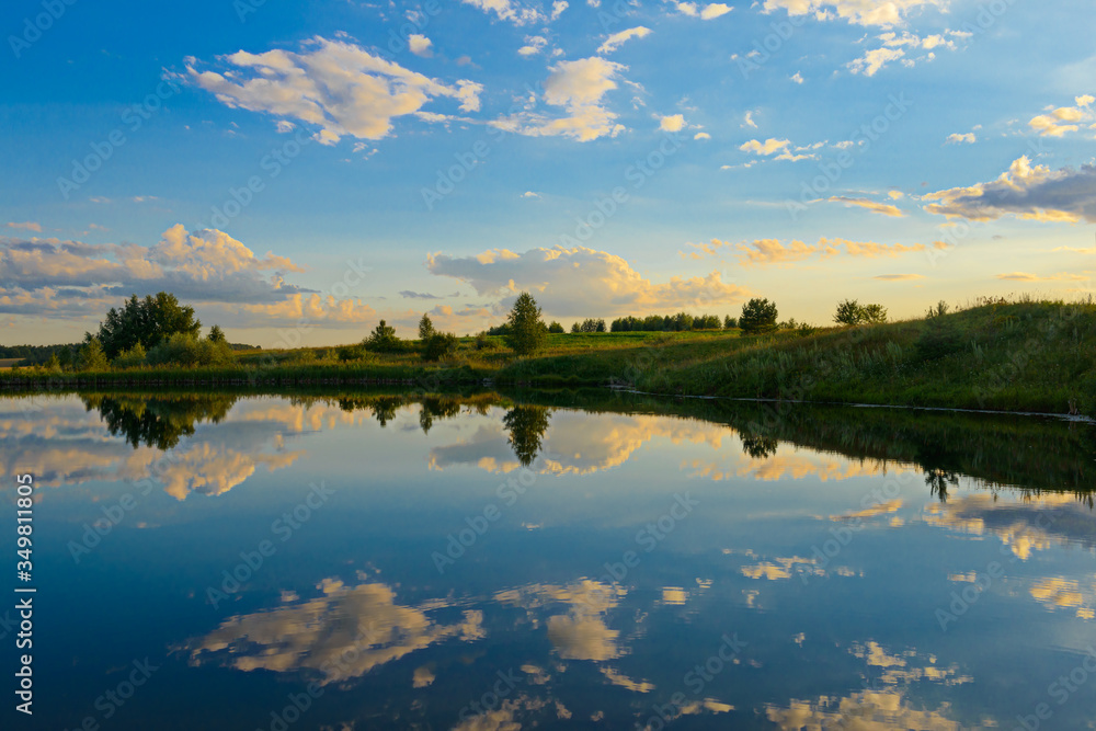 Summer evening landscape with blue sky reflected by clouds in a small lake