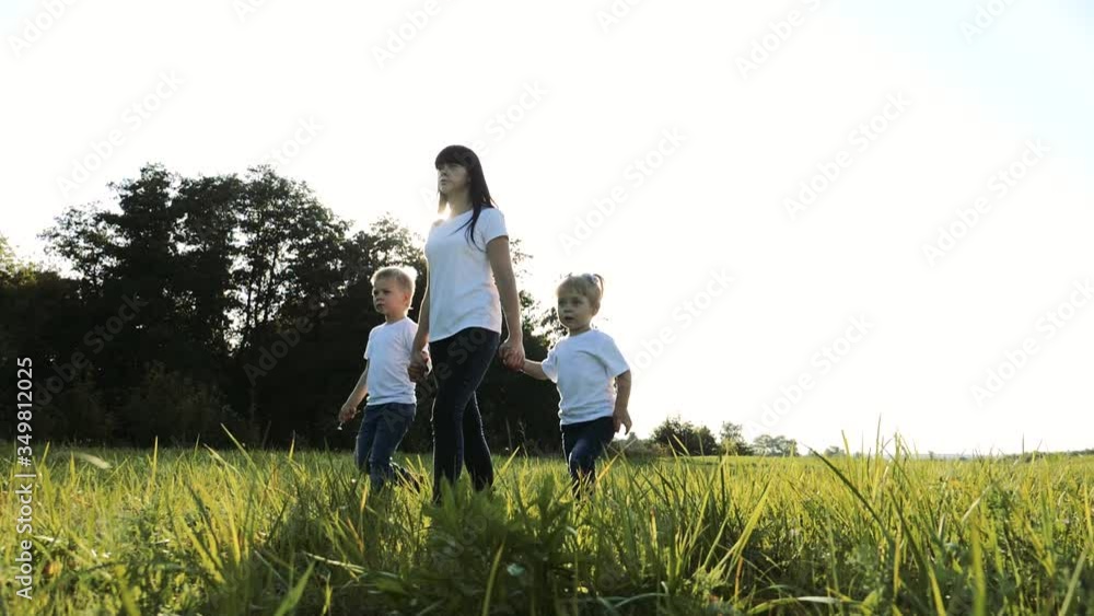 happy family teamwork mother, little brother and sister walk in the park nature holding hands slow motion video concept. mom, kids boy and girl daughter and son lifestyle hold hands go on green grass happy family teamwork mother, little brother and sister walk in the park nature holding hands slow motion video concept. mom, kids boy and girl daughter and son lifestyle hold hands go on green grass
