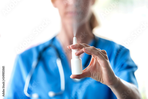 Female doctor with a spray or nasal drops for the treatment of a runny nose over white background.