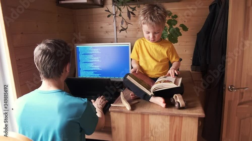 father work at home office, small child sits near and read book, parenthood multitasking, concept of stay home in pandemic quarantine, self-isolated lifestyle, family workplace and workspace
