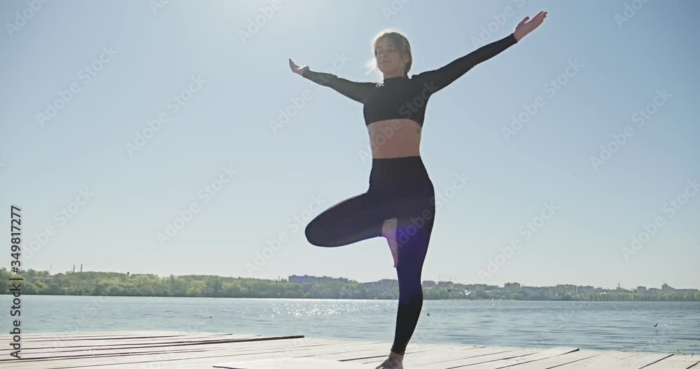 Young Blonde Woman practicing yoga on the wooden berth at lake. Single sport healthy training on nature at sunny weather Young Blonde Woman practicing yoga on the wooden berth at lake. Single sport healthy training on nature at sunny weather