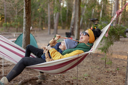 mother hugs her son sitting in a hammock in the forest, laughing and rejoicing, concept happy family camping in the forest