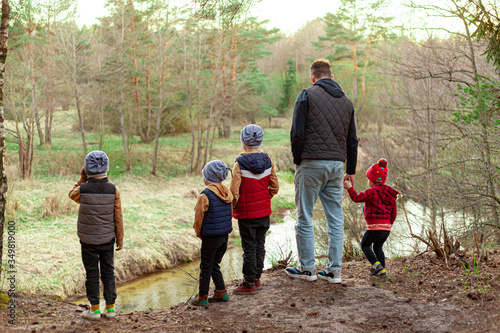 young man and children look at the river from a cliff in the forest, dad and four children, paternity leave © Stockgurulab