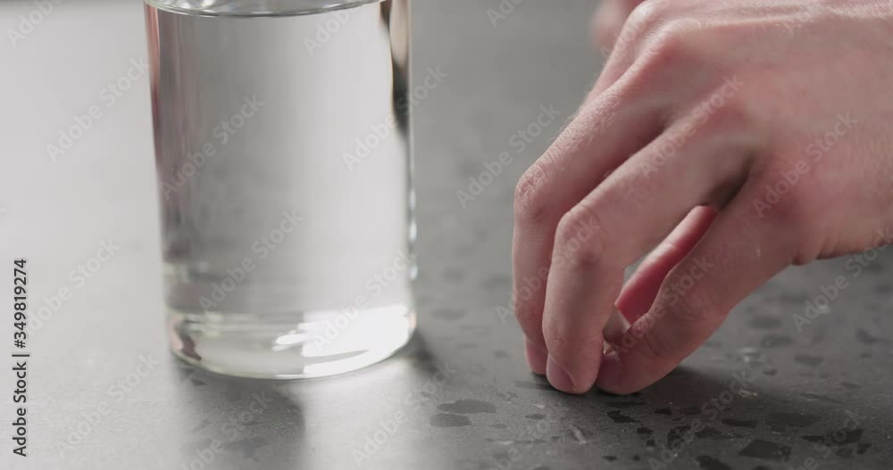 Slow motion man hand put white pills and glass of water on terrazzo countertop Slow motion man hand put white pills and glass of water on terrazzo countertop