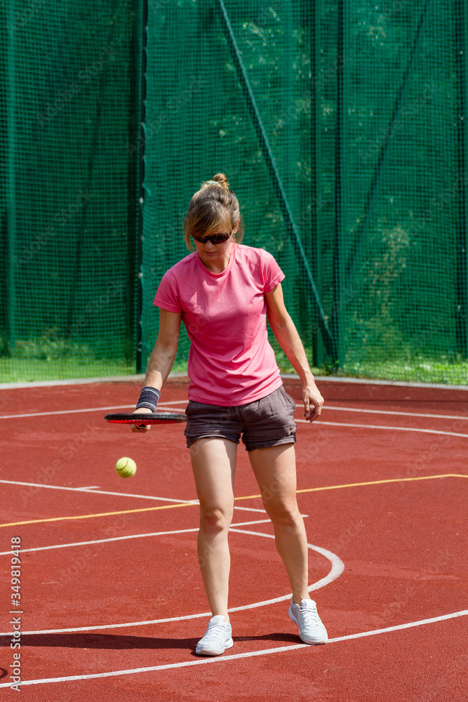 Female tennis player bouncing tennis ball on a court