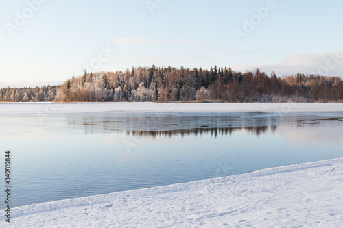 Unfrozen lake with snowy coastline with a forest at background.