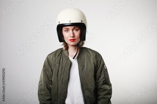 Caucasian biker young woman, wearing retro helmet, with red lips posing over white wall. Space for your text. © face_reader_img