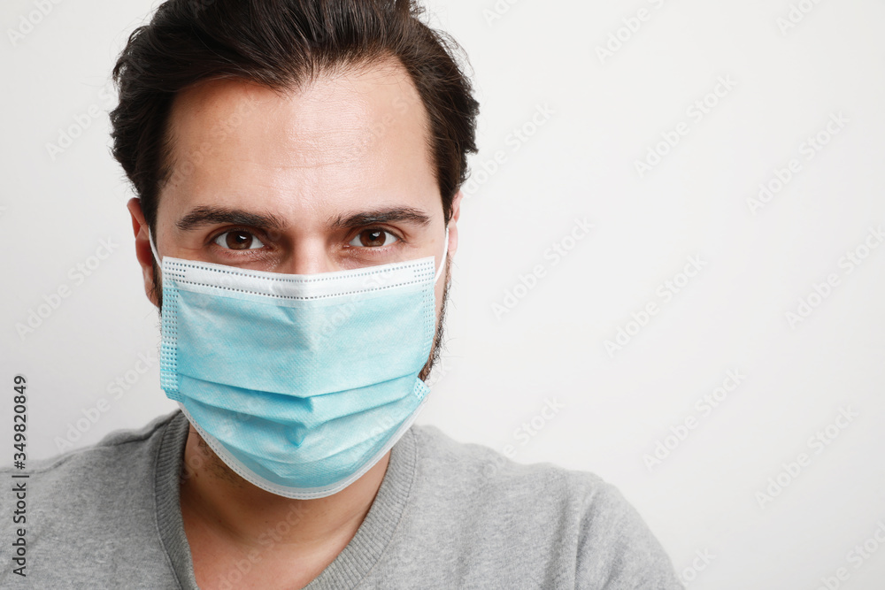 Close-up of young caucasian man in a blue medical virus mask on his face. Theme of coronavirus and safety. Horizontal. Close-up of young caucasian man in a blue medical virus mask on his face. Theme of coronavirus and safety. Horizontal.