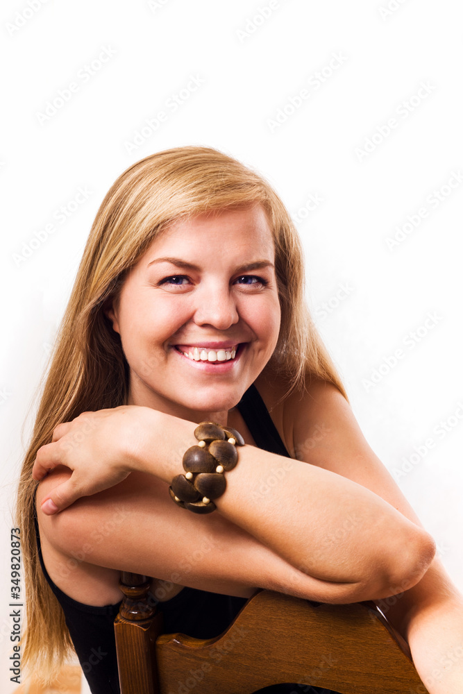 Portrait of a beautiful natural blonde sitting on a chair on a white background. She looks at the camera and smiles.