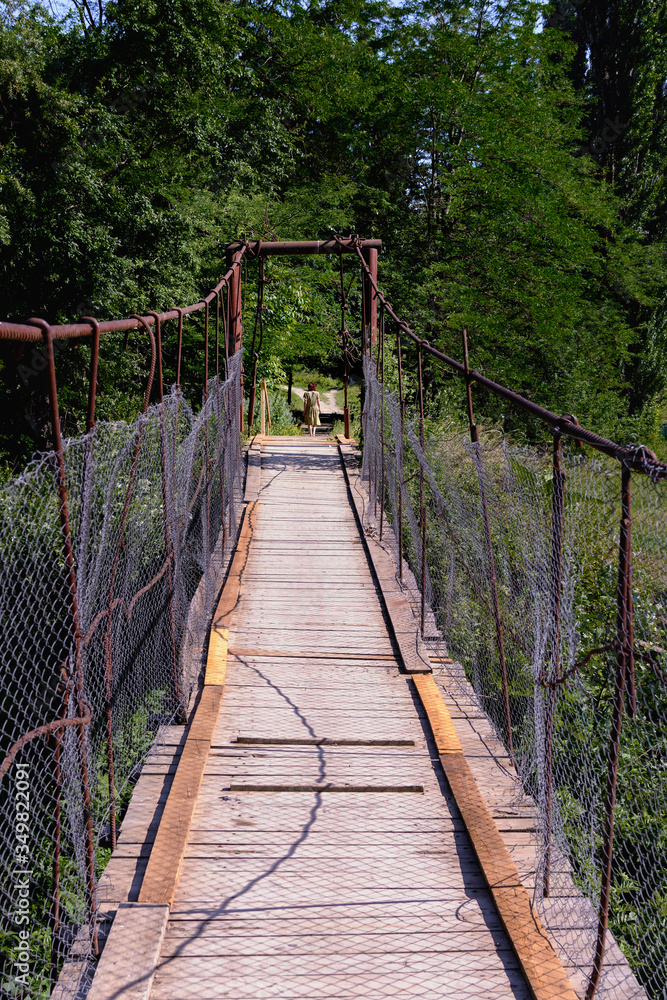 Old suspension bridge over the small river is leading to the forest