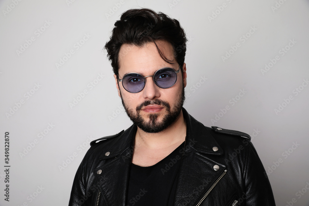 Obraz premium Bearded man in the leather outfit with bright white t-shirt wearing stylish spectacles posing over white wall. Isolated.