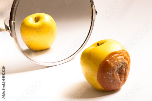 Photo Apple in good condition looking at itself in the mirror while its back is rotten