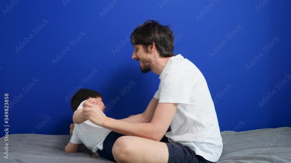 father and son are sitting on the bed playing and having fun jumping father and son are sitting on the bed playing and having fun jumping
