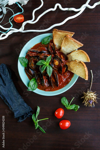 Mussels in tomato sauce with garlic in a blue plate on a brown wooden background