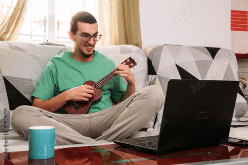 Young man learning to play the ukulele online from his couch