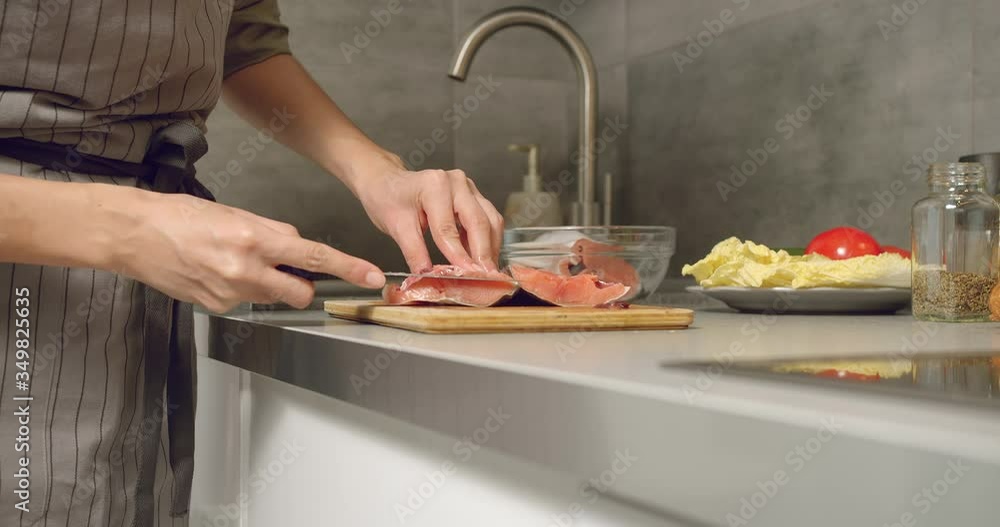 Close up of female hands of a cook cutting a piece of fresh salmon fish on a wooden board in the kitchen. Close up of female hands of a cook cutting a piece of fresh salmon fish on a wooden board in the kitchen.