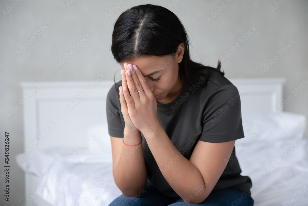 Devout African woman closed eyes folded palms near face prays in morning sitting on bed. Desperate mixed-race female looking unhappy suffers, personal life or health trouble, break up, divorce concept Devout African woman closed eyes folded palms near face prays in morning sitting on bed. Desperate mixed-race female looking unhappy suffers, personal life or health trouble, break up, divorce concept