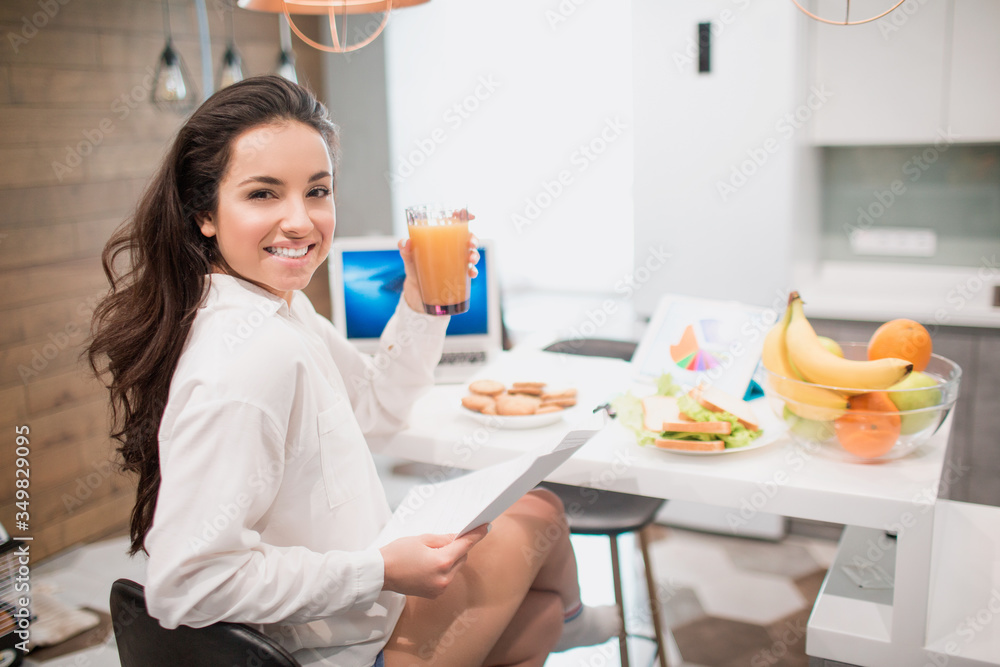 Beautiful black-haired woman works from home. An employee sits in the kitchen and has a lot of work on a laptop and tablet and has video conferencing and meetings.