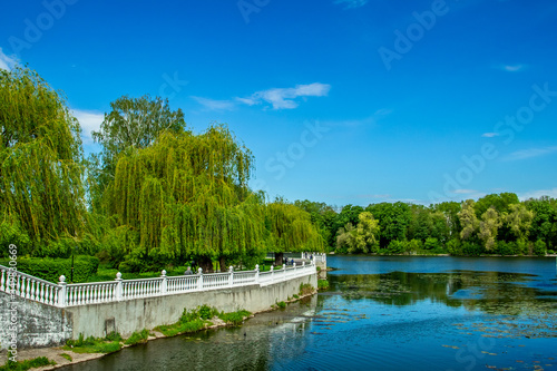 summer nature landscape waterfront walking site city district green foliage trees park and marble fence along river shore line with blue water and sky vivid colorful June day